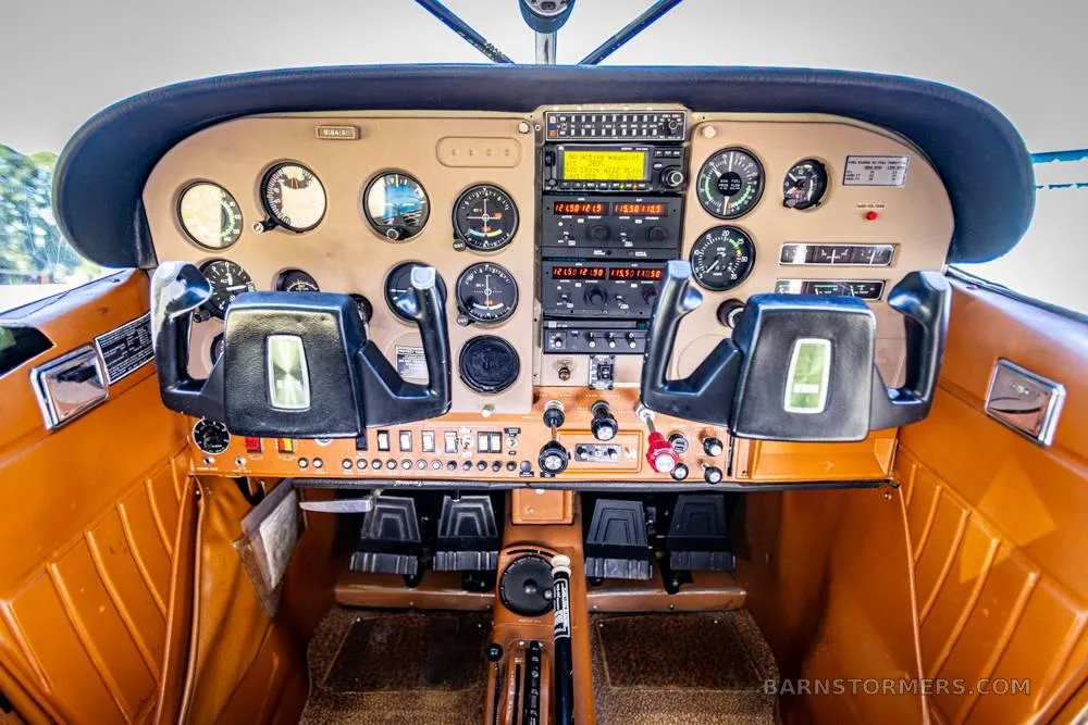 The cockpit of an aircraft with a brown instrument panel, dual yokes, and various gauges and radios.