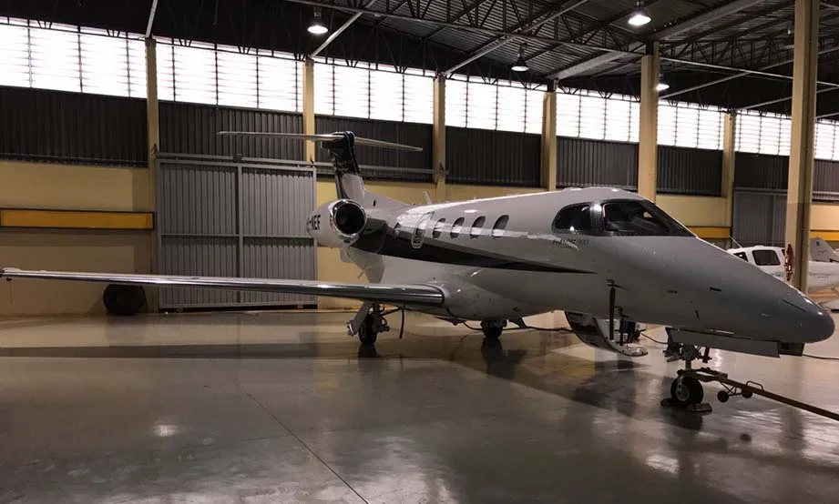 A white Embraer Phenom 300 business jet with black and grey accents is parked inside a hangar.