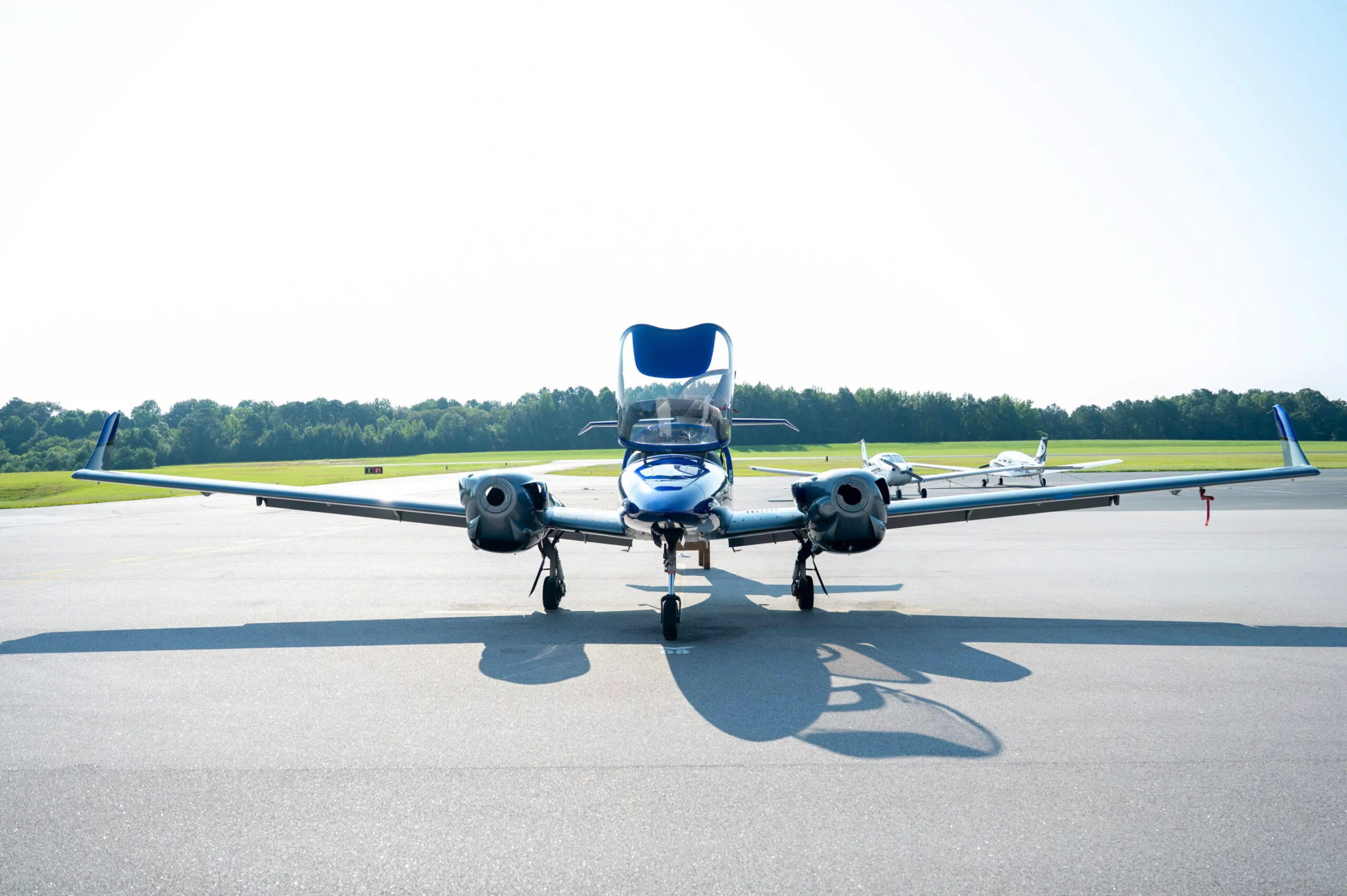 Front view of a blue and grey Diamond DA42 aircraft with doors open, parked on an airfield.