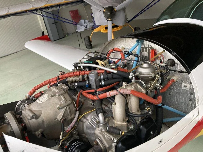 The open engine compartment of a small aircraft, revealing the engine, hoses, and wiring.