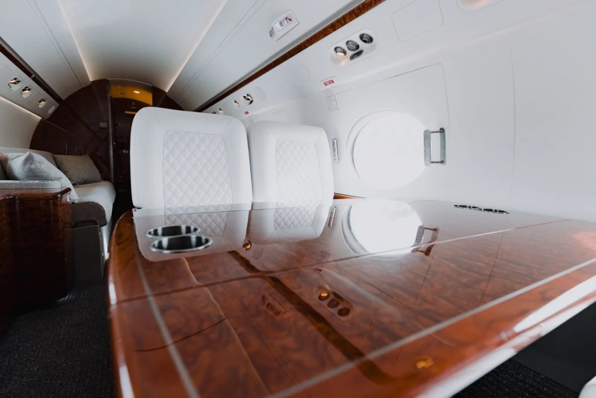 A section of the aircraft cabin with a polished wooden table, white quilted seats, and large windows.