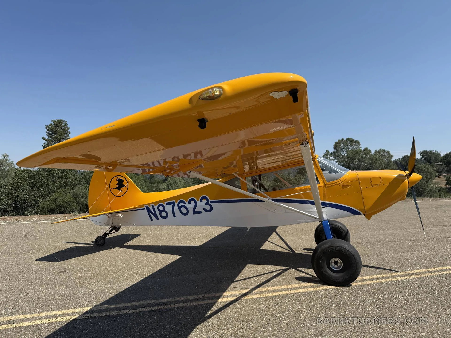 A yellow and white single-engine aircraft with large tires, registration N87623, parked on an asphalt runway under a clear sky.
