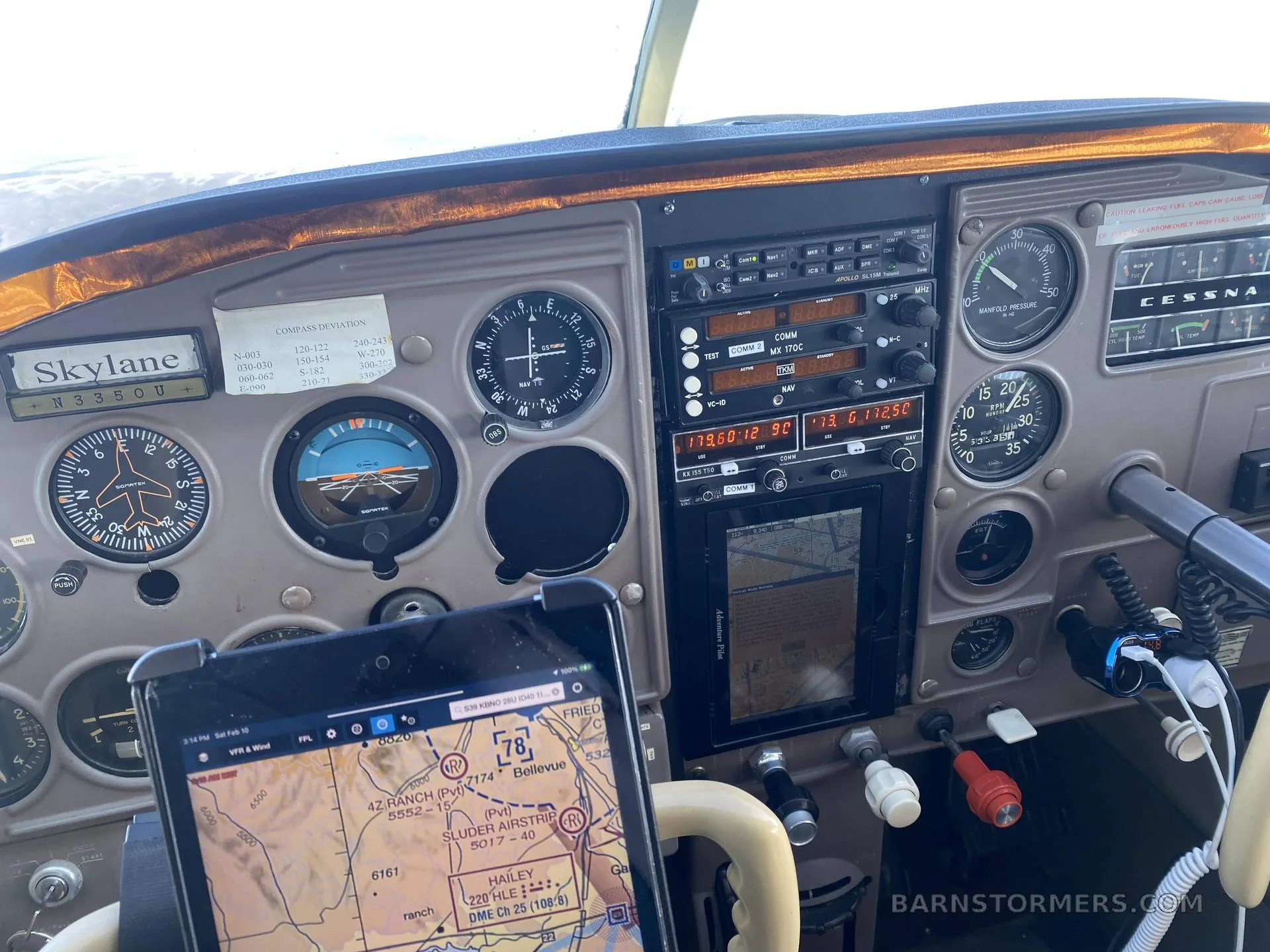 The cockpit instrument panel of a Cessna Skylane, showing gauges, radios, and a tablet displaying an aviation map.