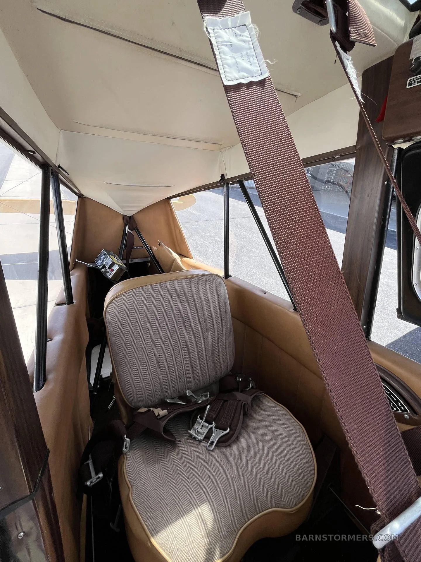 Interior view of an aircraft cabin showing two brown and beige seats with seatbelts, and a light-colored ceiling.