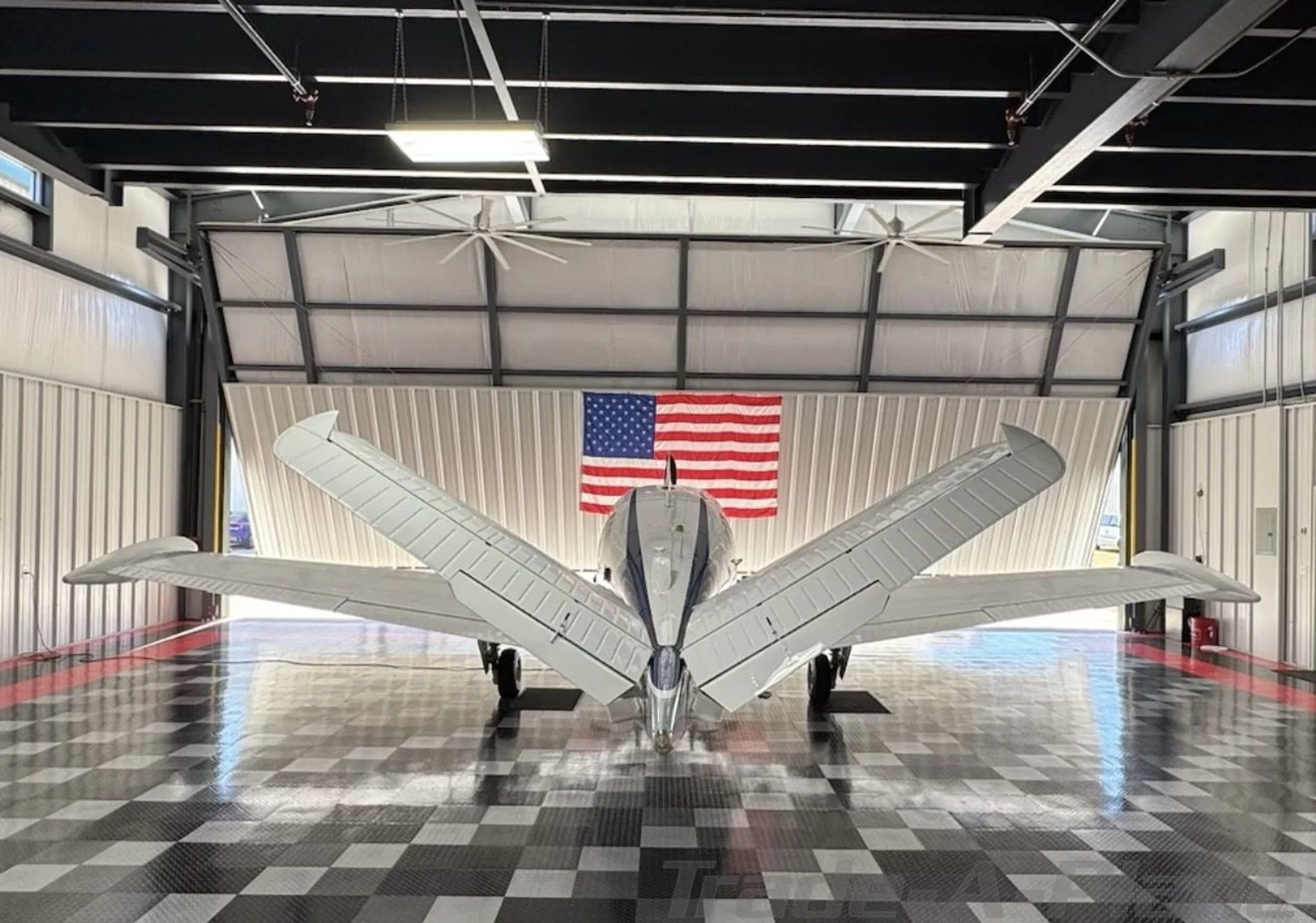 A rear view of a white Beechcraft Bonanza N35KJ with its distinctive V-tail in a hangar.