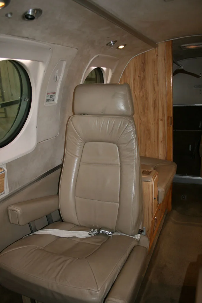 A tan leather passenger seat in the aircraft cabin, with wood paneling and a large oval window.