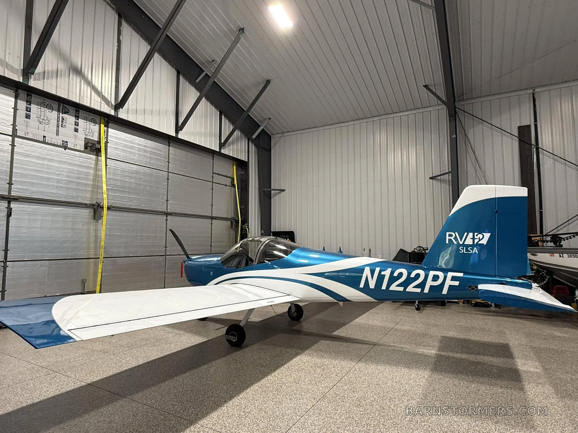 A blue and white RV-12 SLSA aircraft (N122PF) is parked inside a metal hangar.
