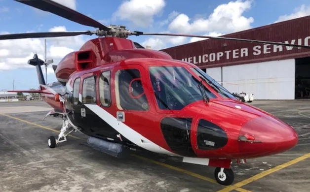 A red, black, and white AgustaWestland AW139 helicopter parked on a tarmac in front of a hangar.