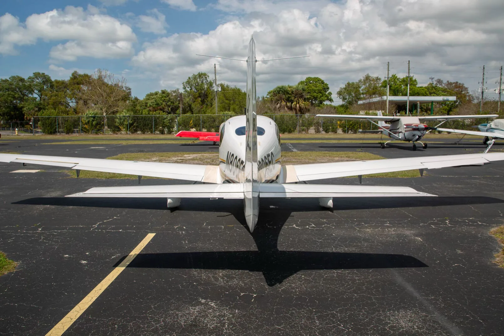 A white Cirrus SR22 aircraft, registration N806EC, seen from the rear on an airport tarmac with other planes in the distance.