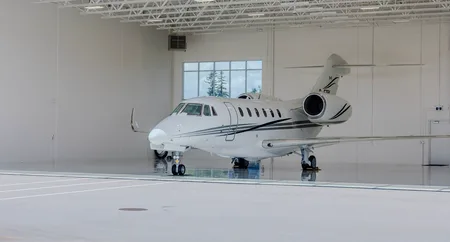 A white business jet with black and grey stripes is parked inside a bright, modern hangar.