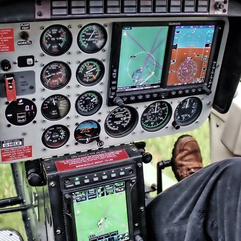 The instrument panel of a helicopter with analog gauges and two Garmin digital displays.