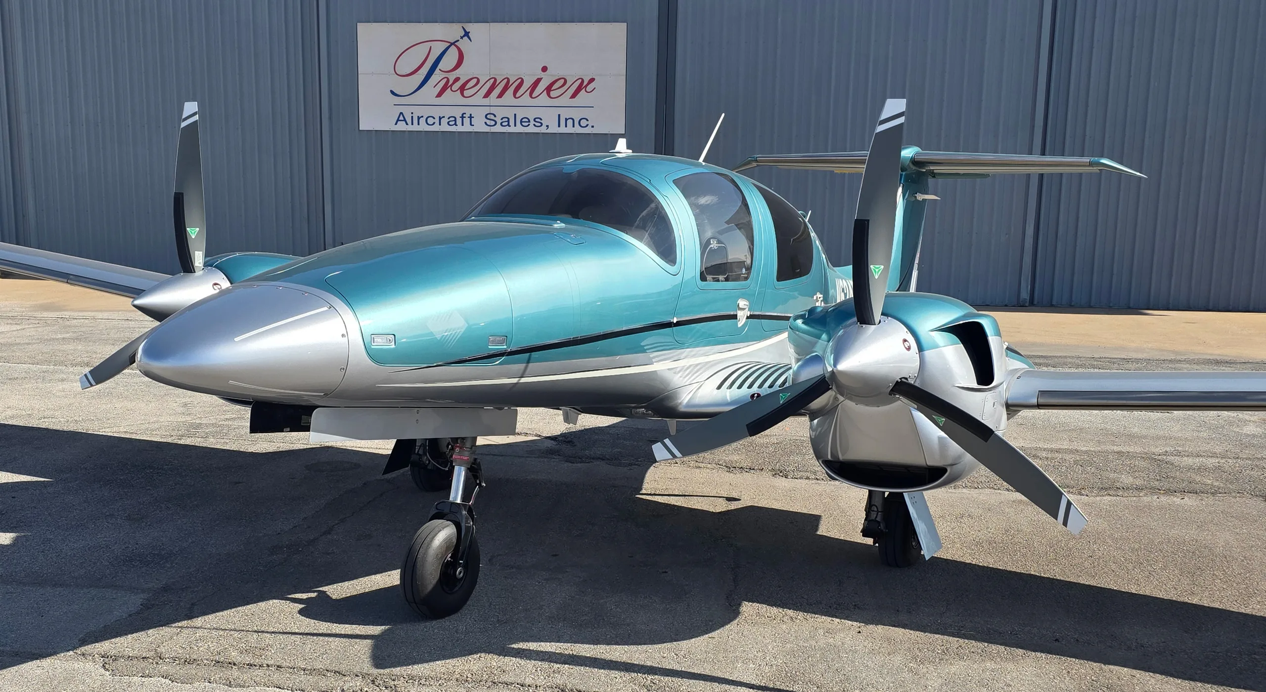 A close-up front three-quarter view of a teal and silver Diamond DA62 twin-engine aircraft on an asphalt ramp.