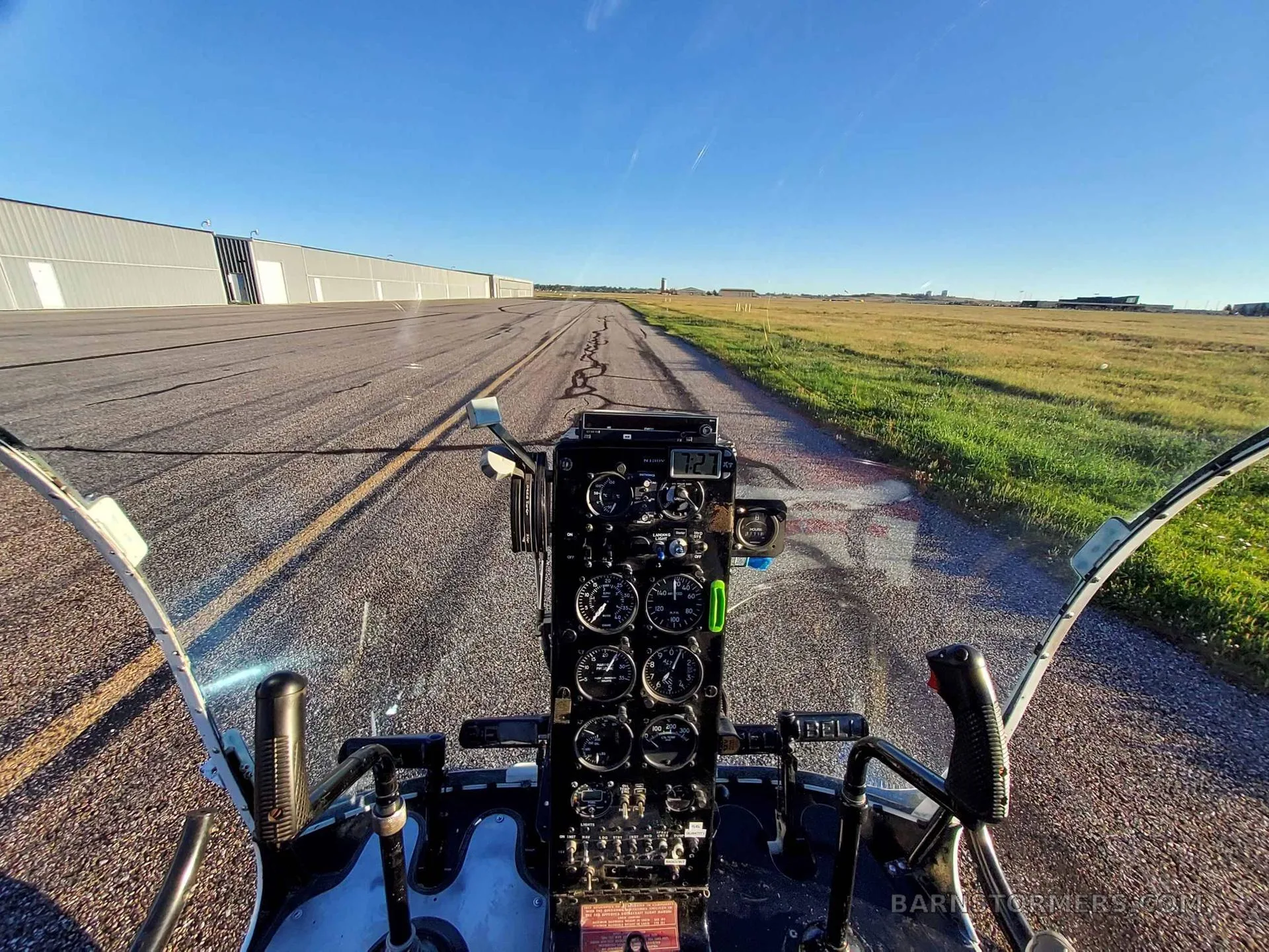 A view from the cockpit of a helicopter, showing the instrument panel and a runway stretching into the distance.