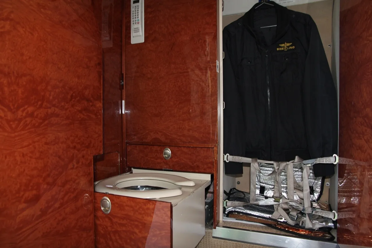 A private jet lavatory with wood paneling and a small closet containing a black jacket.