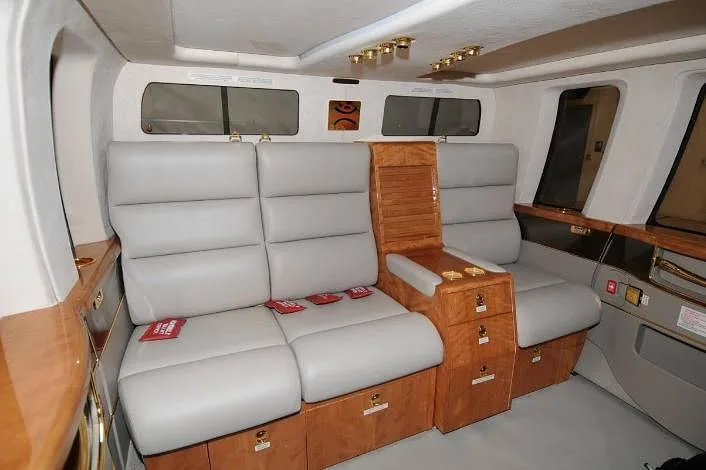 A wide shot of the helicopter's executive interior, featuring light gray seating, a wooden console, and large windows.