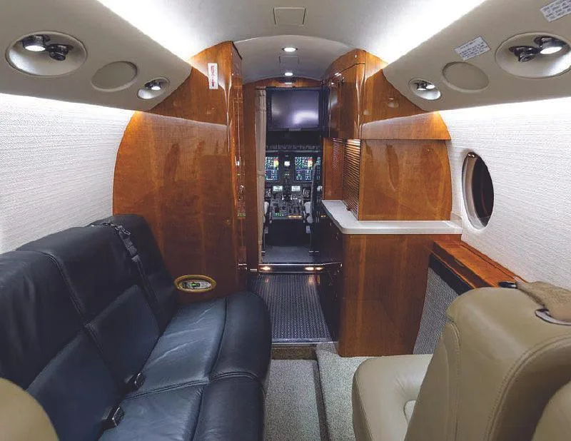 View from the aircraft cabin looking forward, showing black and tan leather seats and a glimpse of the cockpit.