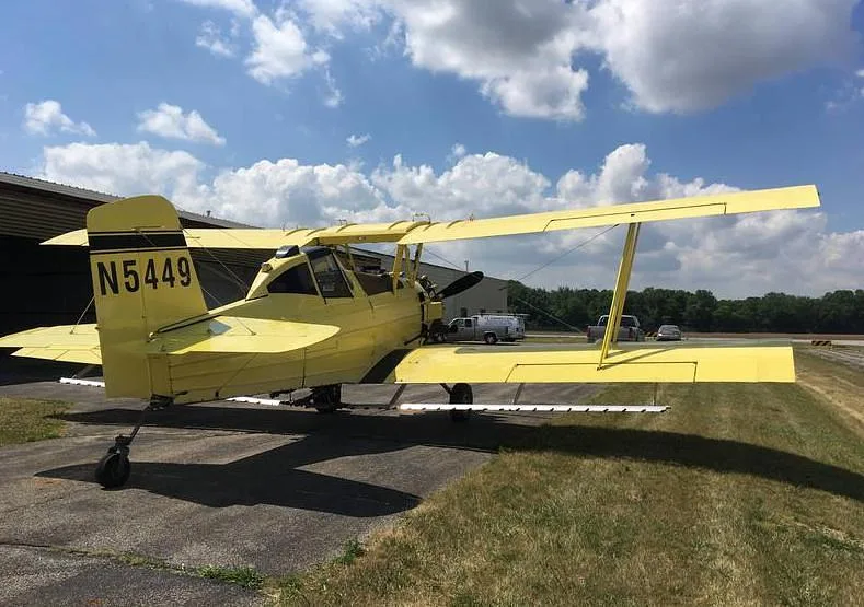 A yellow biplane crop duster, N5449, seen from the rear-left on an airfield.