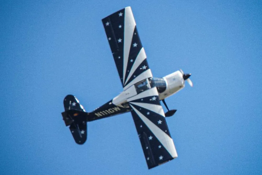 A black and white biplane with a starburst paint scheme, registered N111GW, flying against a clear blue sky.