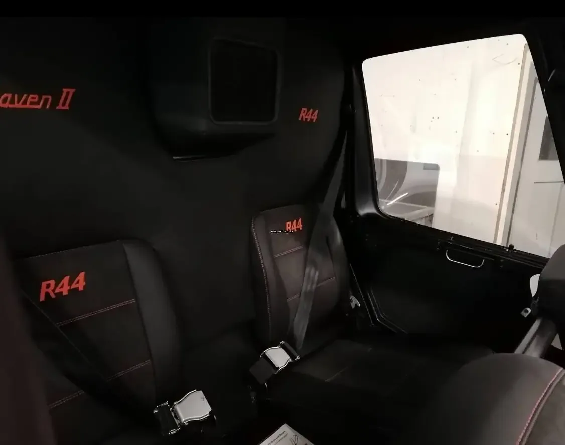 The black leather rear seats of a helicopter cabin with red stitching and "R44 Raven II" branding.