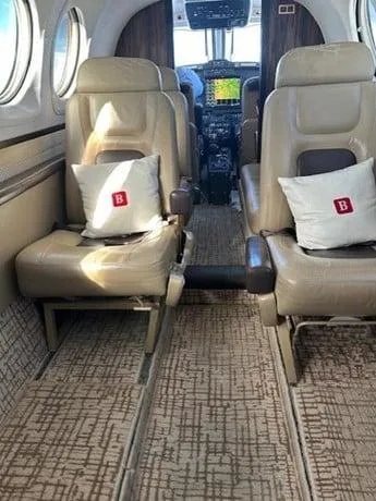 The interior cabin of a private aircraft features tan leather seats with white pillows, looking forward towards the cockpit.