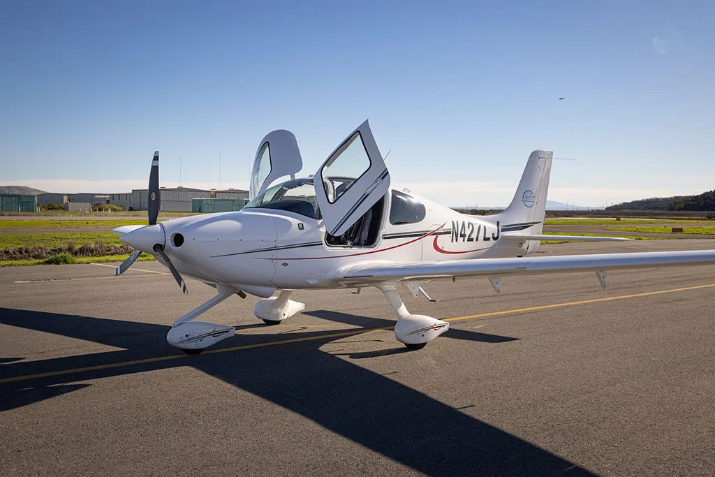 A white single-engine aircraft, N427LJ, with its gull-wing doors open, parked on an asphalt runway.
