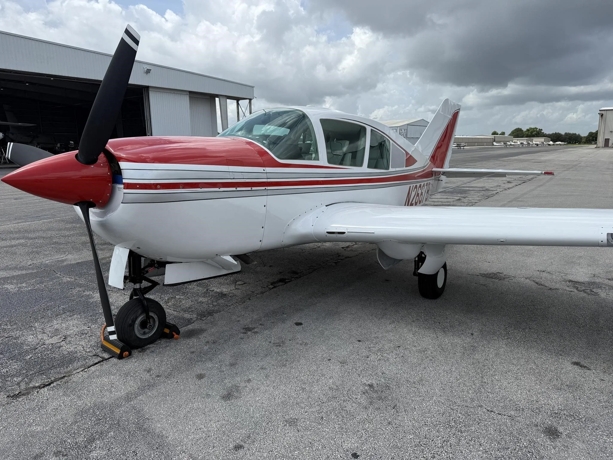 A front-left view of the white and red single-engine aircraft, N2667B, on an airport tarmac.