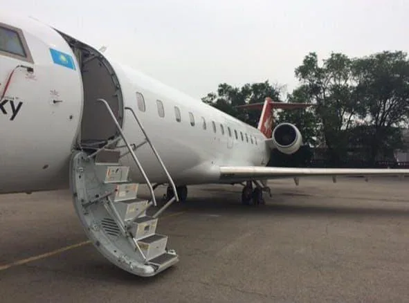 A white regional jet with a blue and yellow flag on its nose and a red tail, with its main passenger door open and integrated stairs extended.