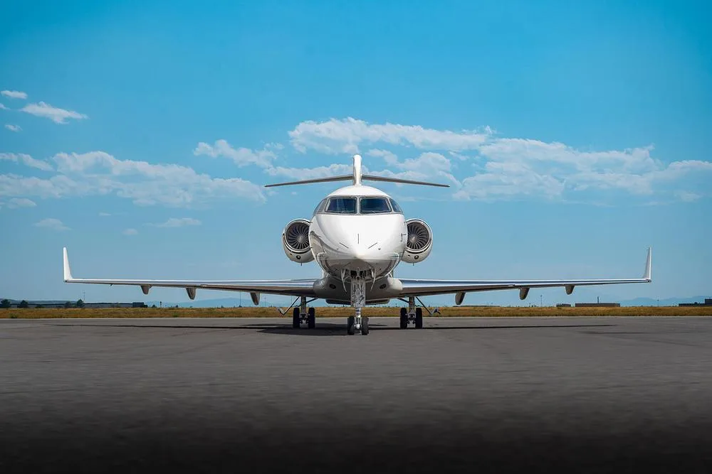 A head-on view of a white Bombardier Challenger 300 business jet with two engines, parked on an asphalt tarmac.