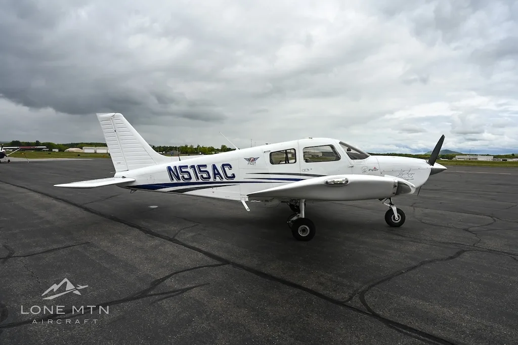 A white single-engine propeller aircraft with blue accents, registration N515AC, parked on an asphalt tarmac under a cloudy sky.