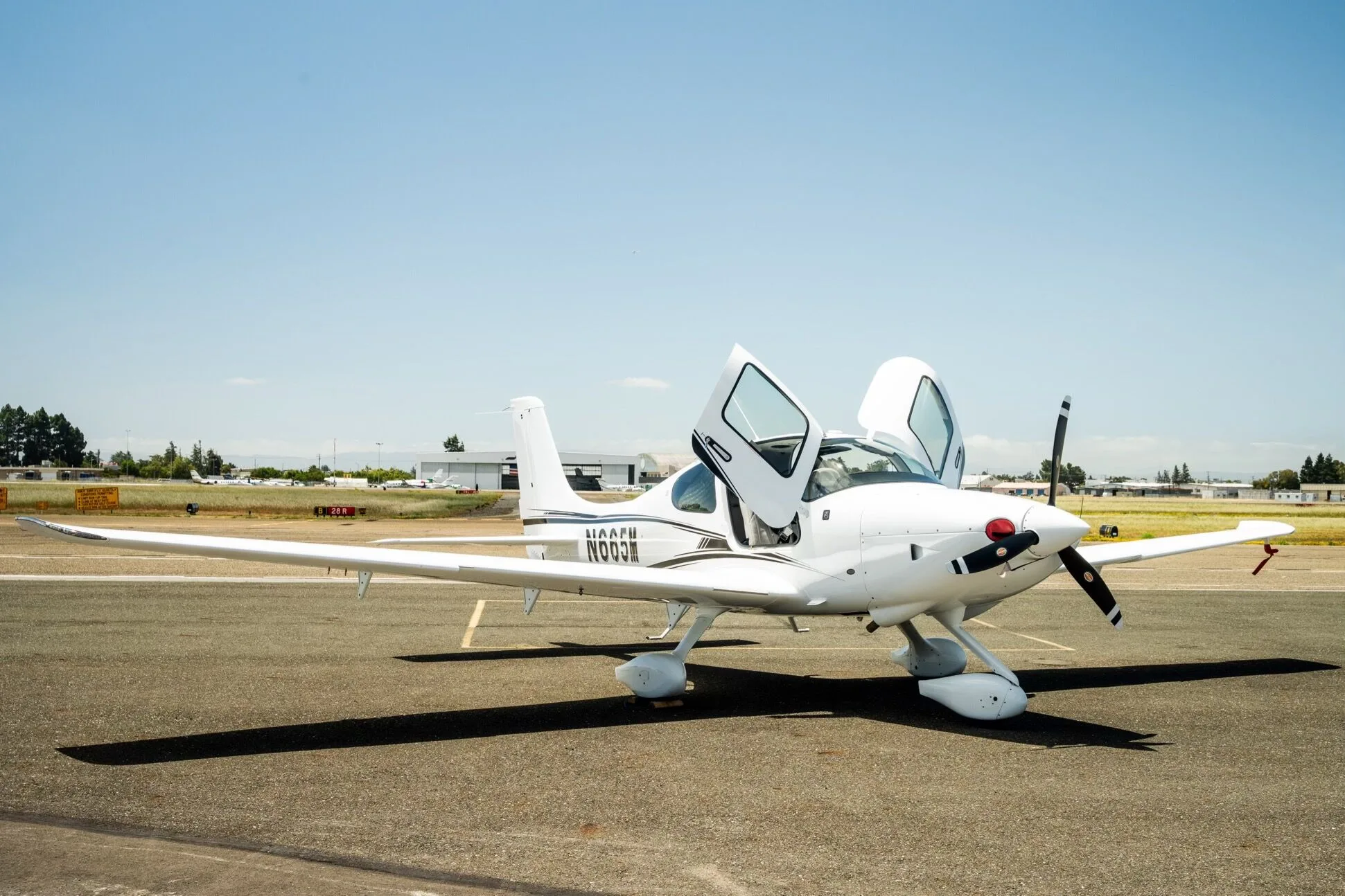 A white Cirrus SR22 aircraft with registration N665M parked on the tarmac with both doors open, viewed from the front.