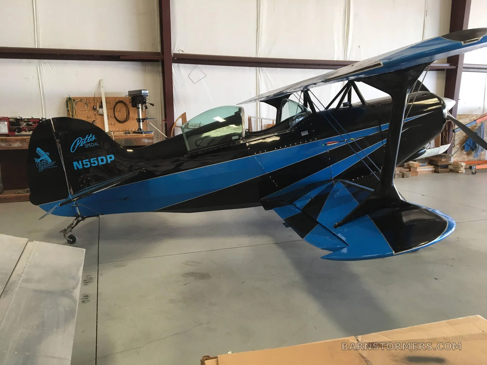 A black and blue Pitts Special biplane, tail number N55DP, is parked inside a hangar.