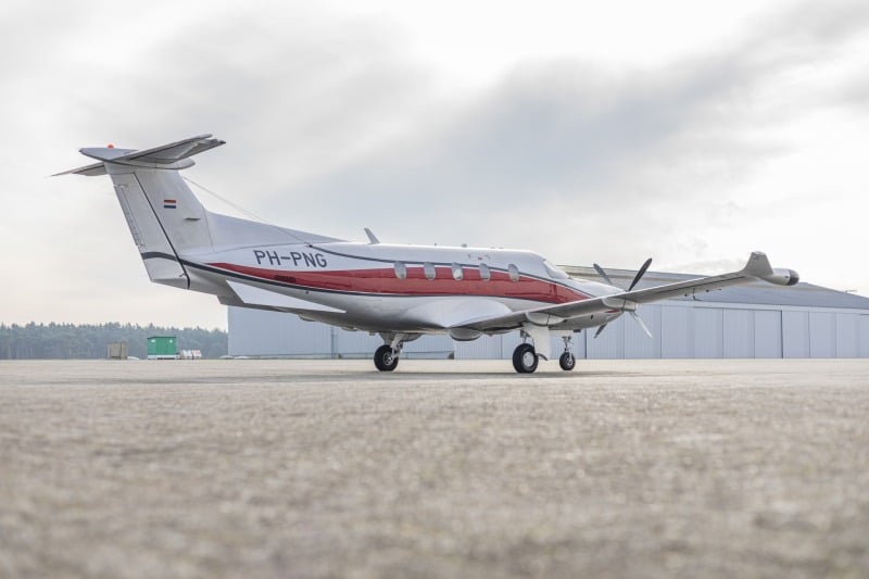 A Pilatus PC-12 aircraft with a silver and red paint scheme, registration PH-PNG, parked on the tarmac.
