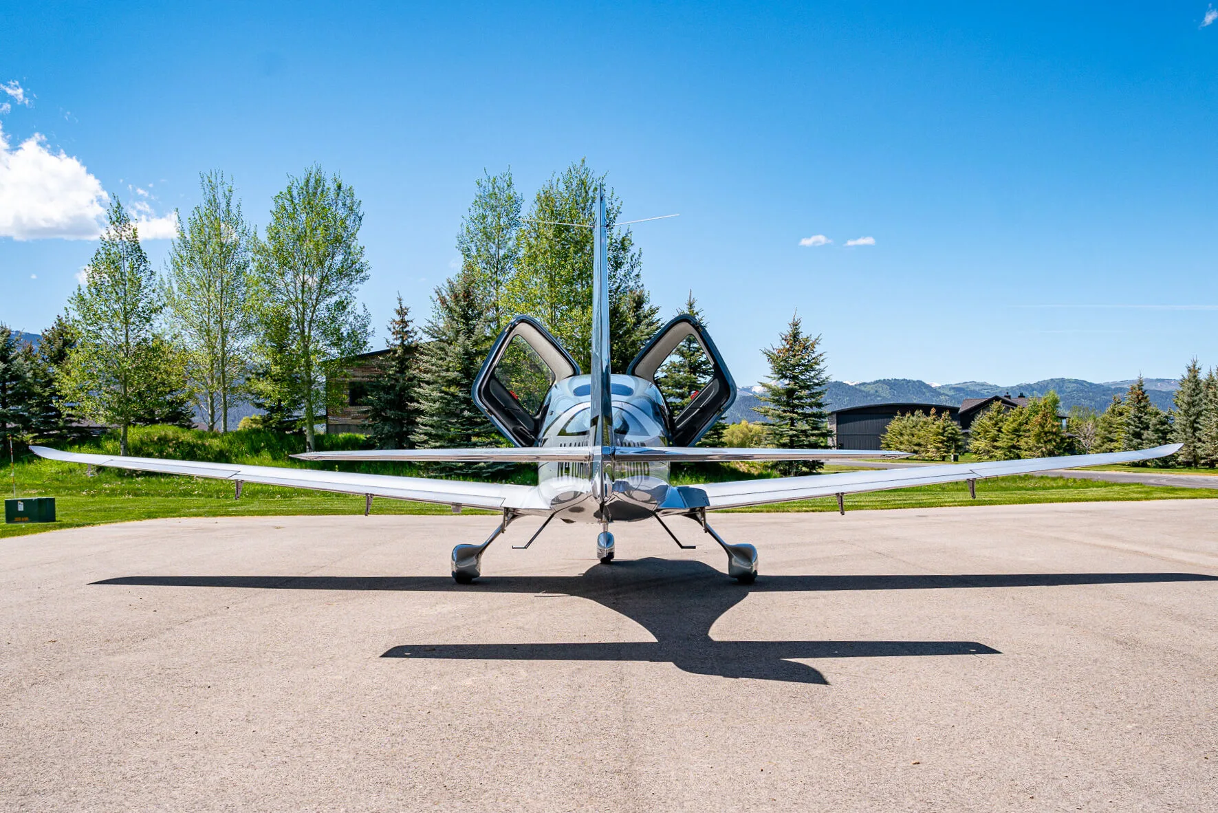 Rear view of a light blue and silver Cirrus SR22T aircraft with its doors open, parked on an airfield.