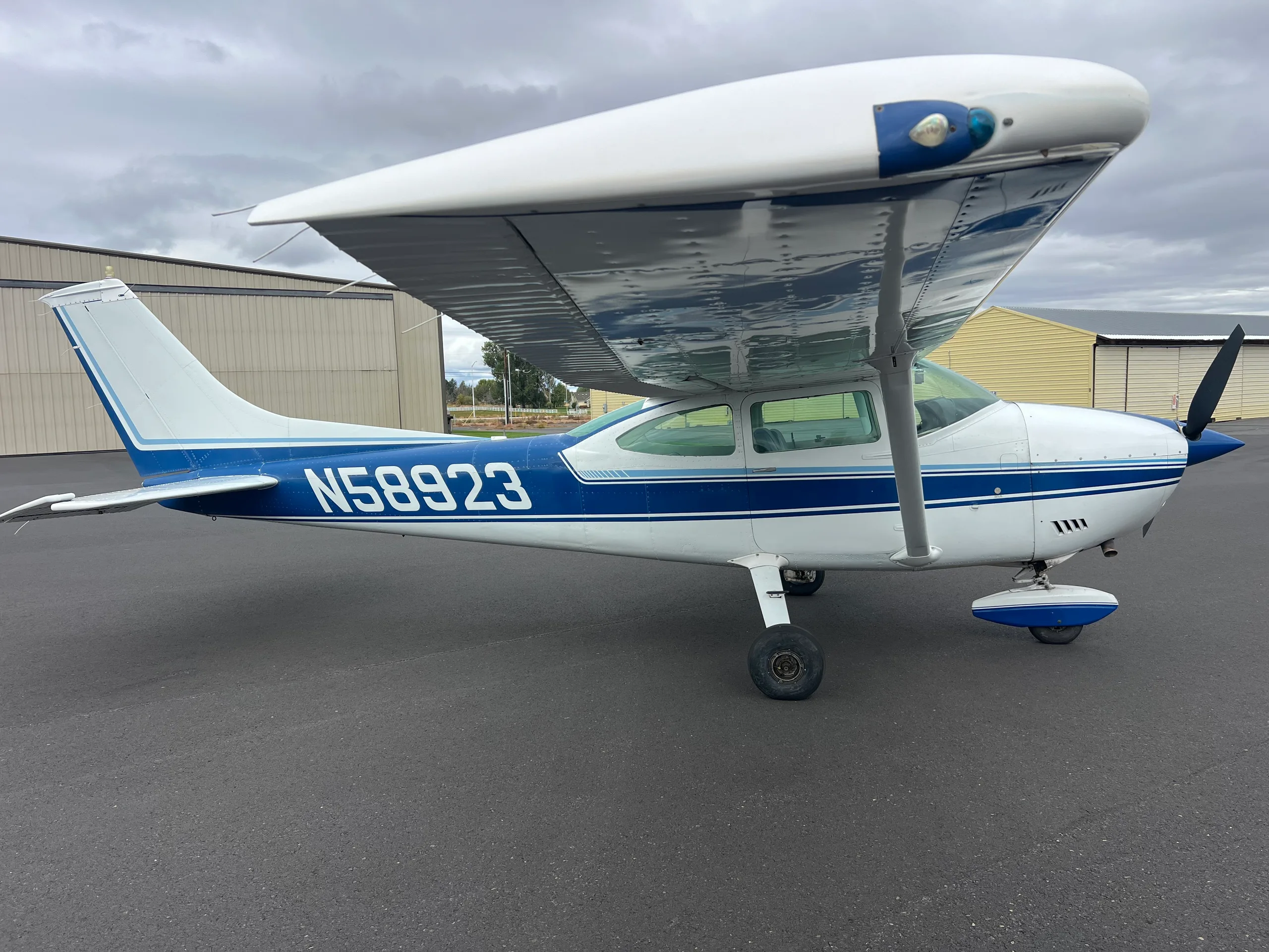A blue and white Cessna 172 aircraft, N58923, parked on an asphalt tarmac under a cloudy sky.