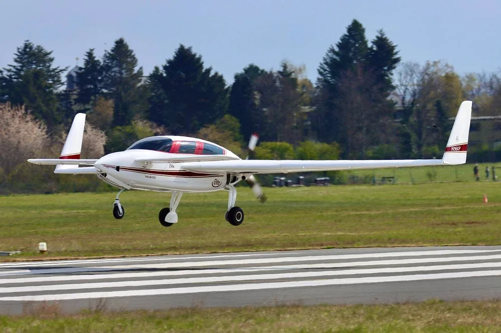 A white Velocity Elite aircraft with red and gold stripes, registration N96KP, landing on a runway.