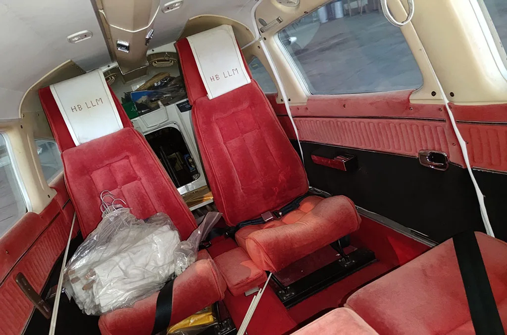 The aircraft's red upholstered cabin seats are visible, with some items on the floor and a view into the cockpit area.