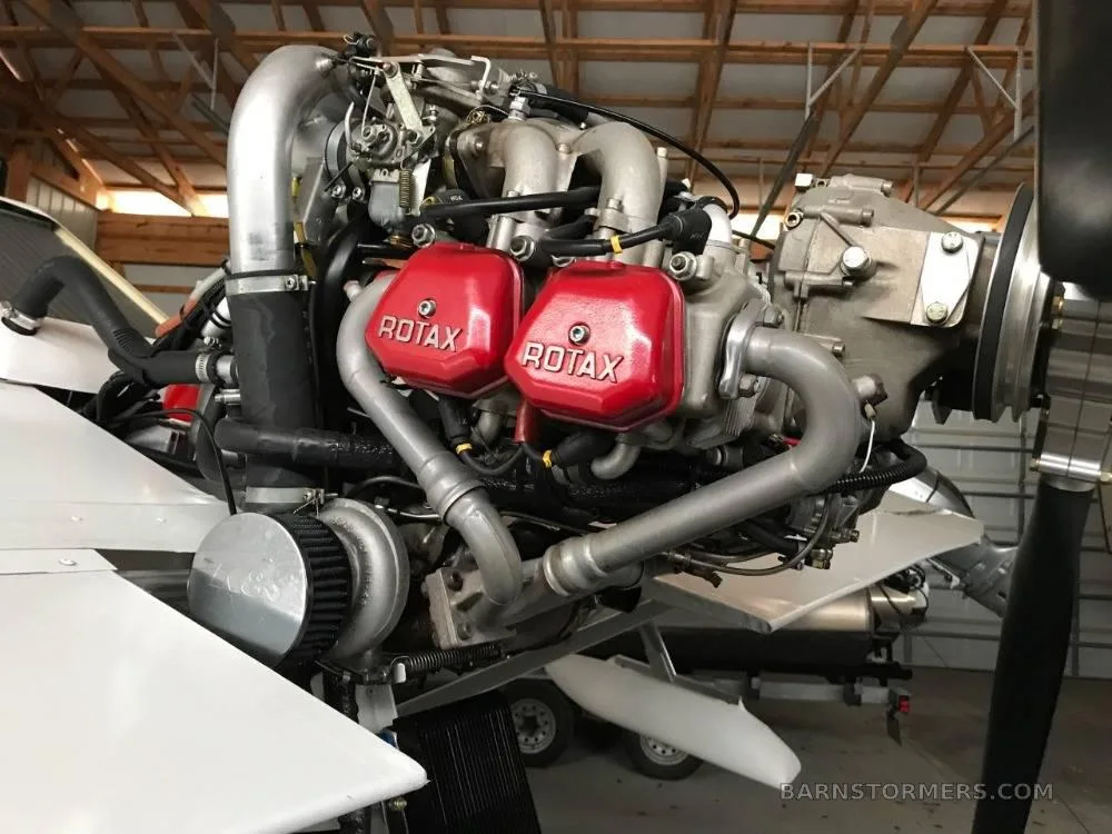 A close-up view of a Rotax aircraft engine with red valve covers, mounted on a white aircraft wing.