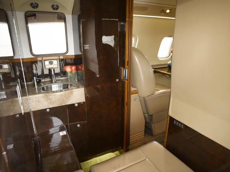 View of the aircraft lavatory or galley area with a sink, mirror, polished wood cabinetry, and a glimpse of the main cabin.