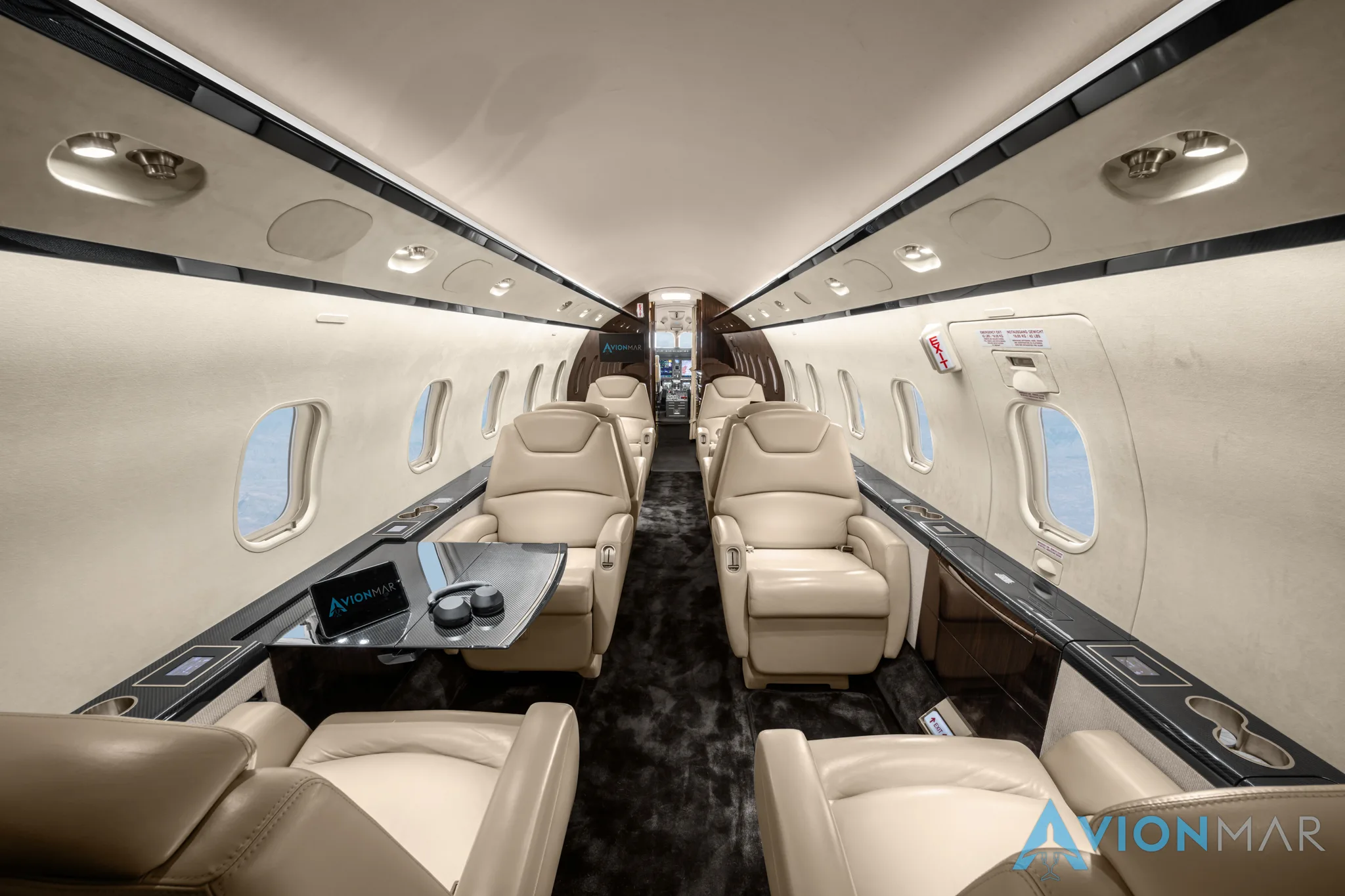 A wide view of the luxurious private jet cabin interior with cream leather seats and a table with headphones.