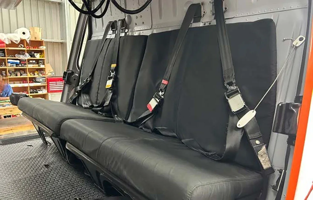 Three black passenger seats with seatbelts visible inside the cabin of a helicopter.
