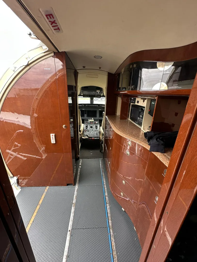 The aircraft's entry area with a galley featuring wooden cabinetry, looking down the aisle towards the cockpit.