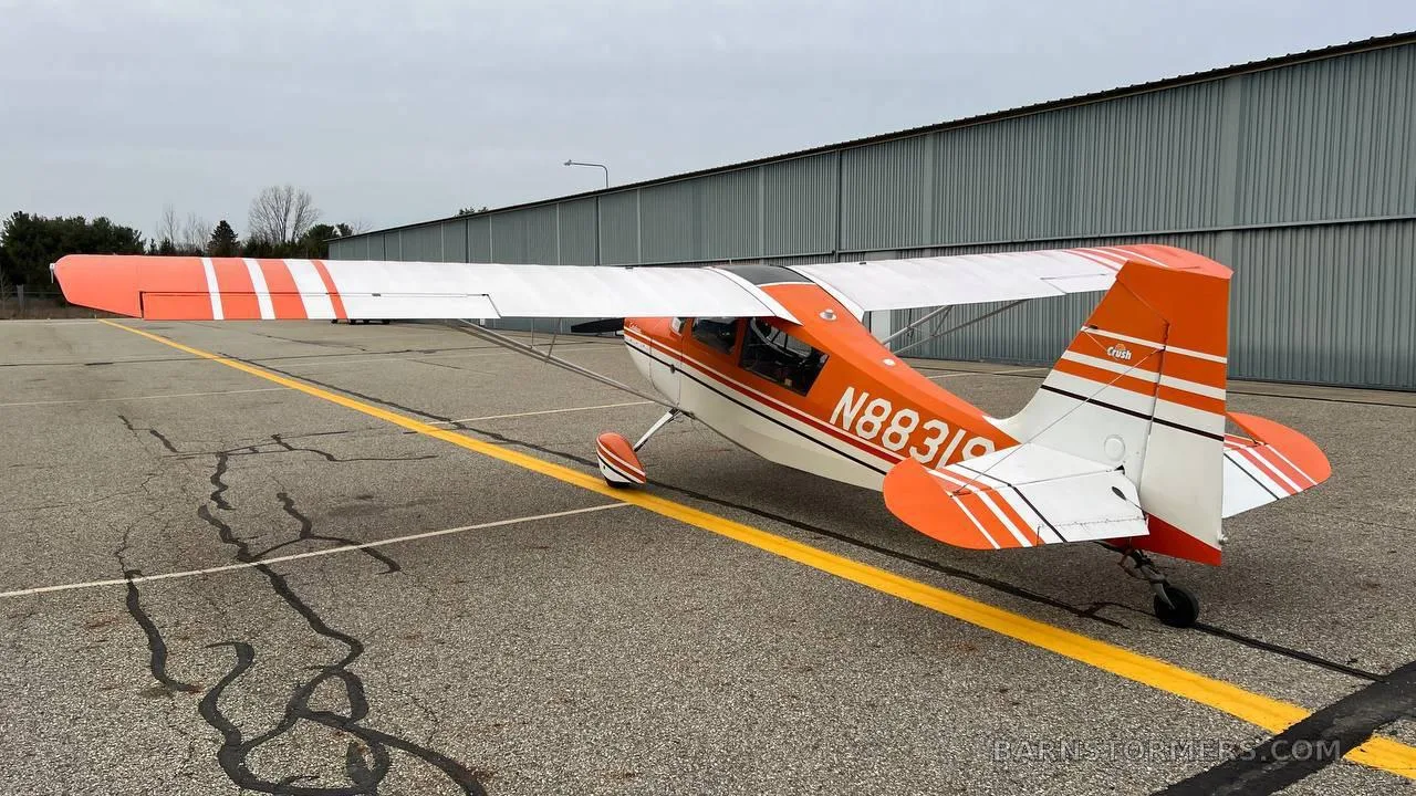 A three-quarter rear view of an orange and white Cessna 170B aircraft with tail number N88319 parked on an asphalt apron.