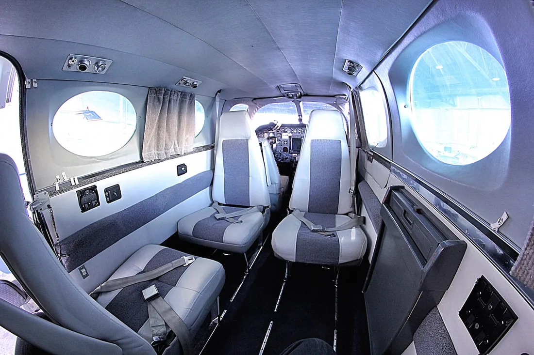 Aircraft interior with gray and white seats and round windows.