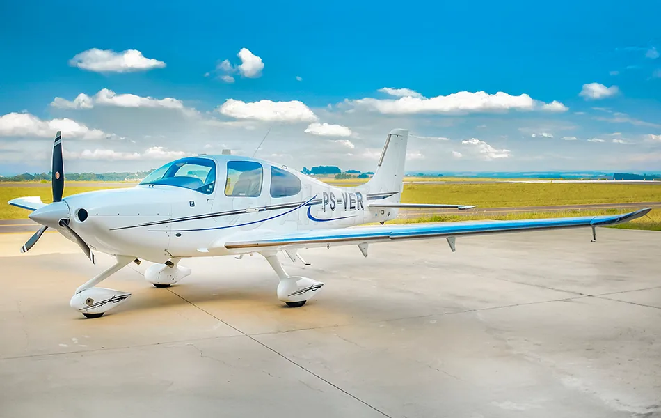 A white single-engine propeller aircraft with blue and black stripes, registration PS-VER, parked on an apron under a blue sky.