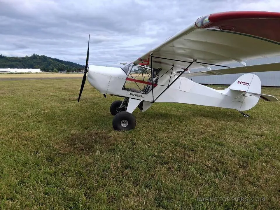 A white experimental aircraft with red accents on the wing and tail, registration N416DD, parked on a grassy field under a cloudy sky.