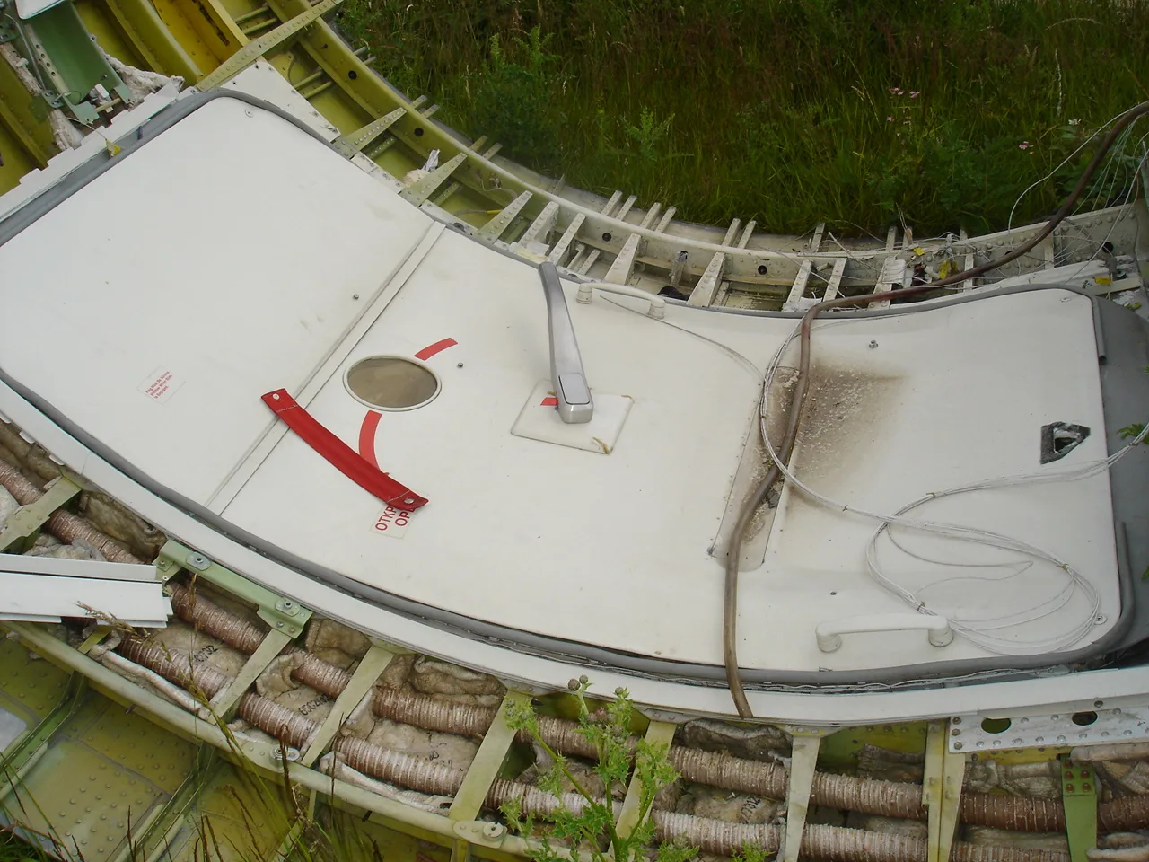 An overhead view of a disassembled aircraft fuselage section showing an emergency exit door and internal insulation.