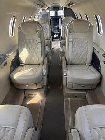 The interior cabin of a private jet, featuring light tan leather seats with diamond stitching arranged in a club configuration.