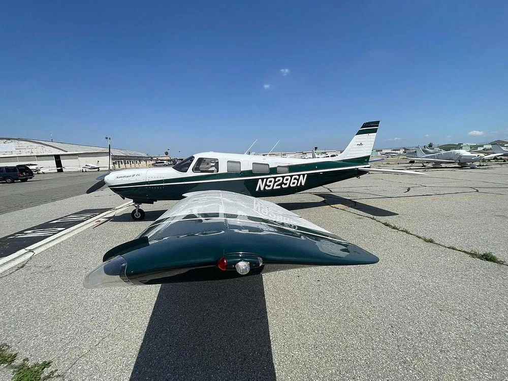 A Piper Saratoga II TC, registration N9296N, in dark green and white, parked on an airfield with one wing covered.