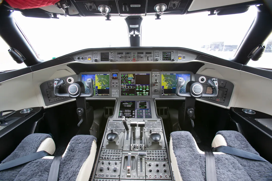 A wide view of a modern aircraft cockpit with multiple digital displays and control yokes.