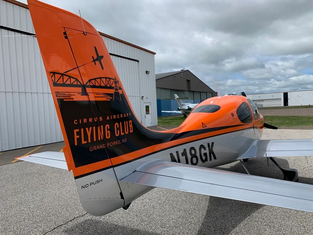 Close-up of the tail of a Cirrus SR20 aircraft, showing the N18GK registration and 'Cirrus Aircraft Flying Club' logo.